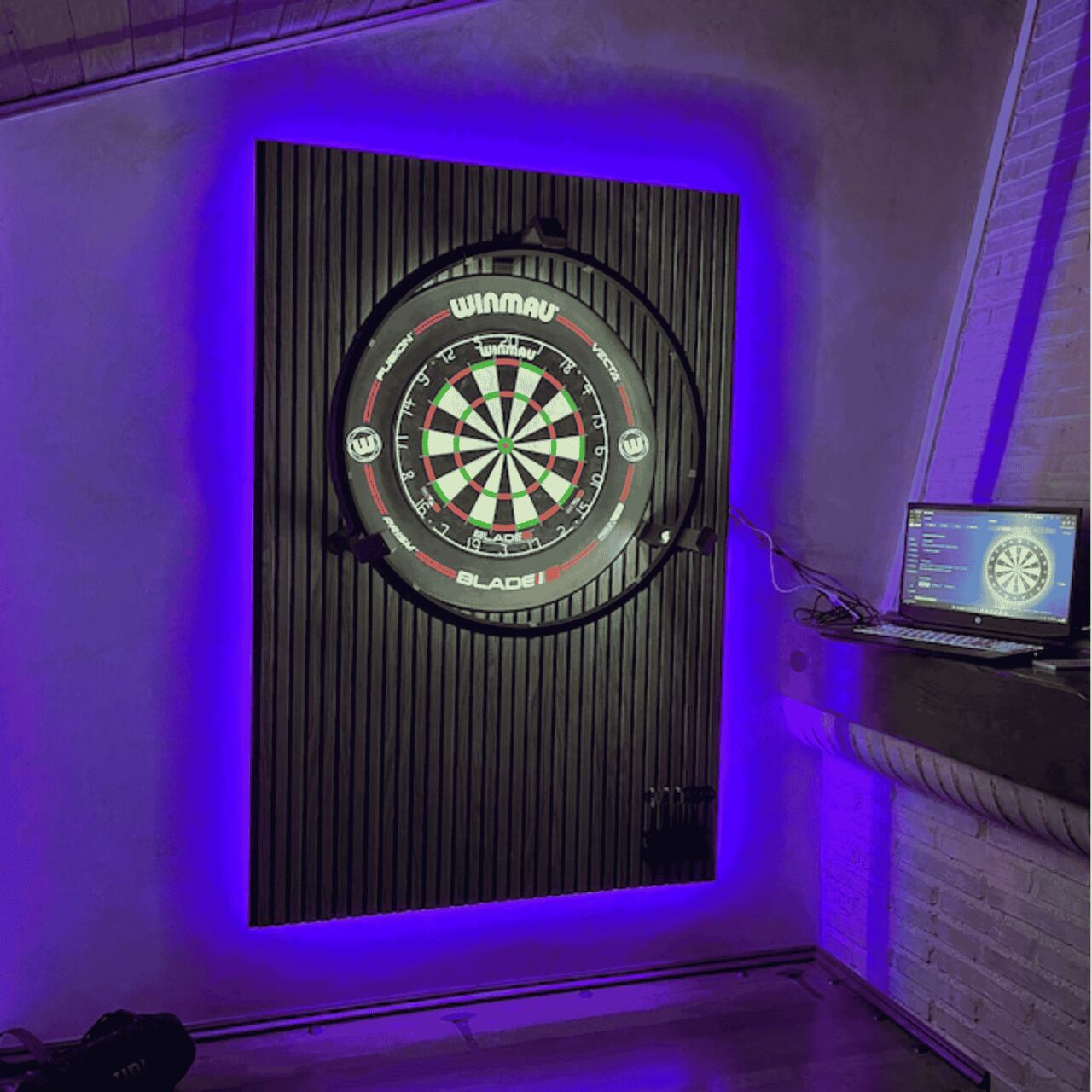 Autodarts Setup mit Winmau Blade Dartboard an Akustikpaneelen mit blauer LED-Hintergrundbeleuchtung und Laptop